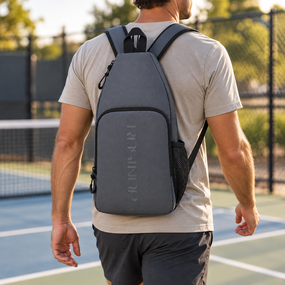 ROSINOP gray pickleball bag worn as a two-strap backpack beside an outdoor court
