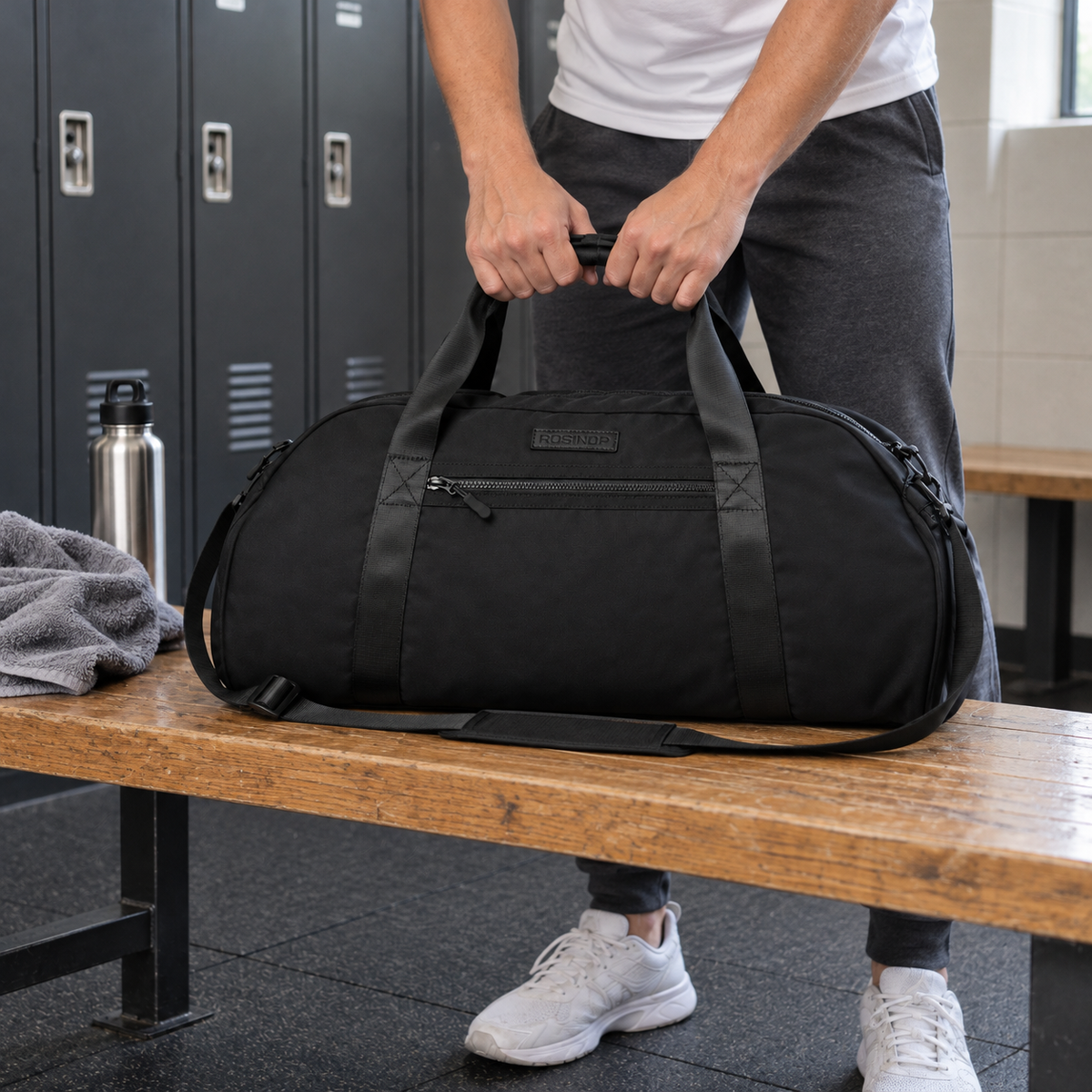 Traveller lifting the black ROSINOP gym duffel from a changing-room bench.