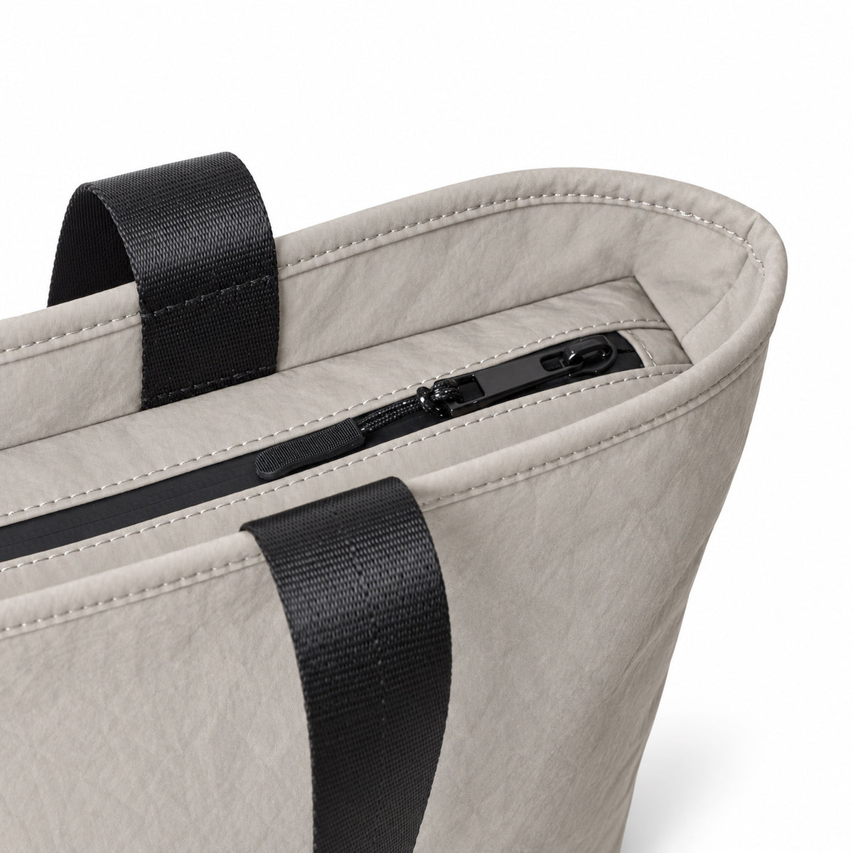 Close-up of the gray tote zipper, stitching and black carry handles.