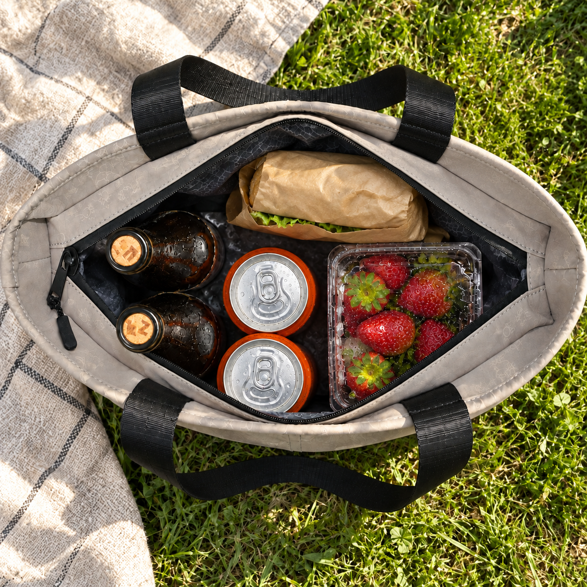 Top-down view of the open gray tote packed with drinks, strawberries and a sandwich.