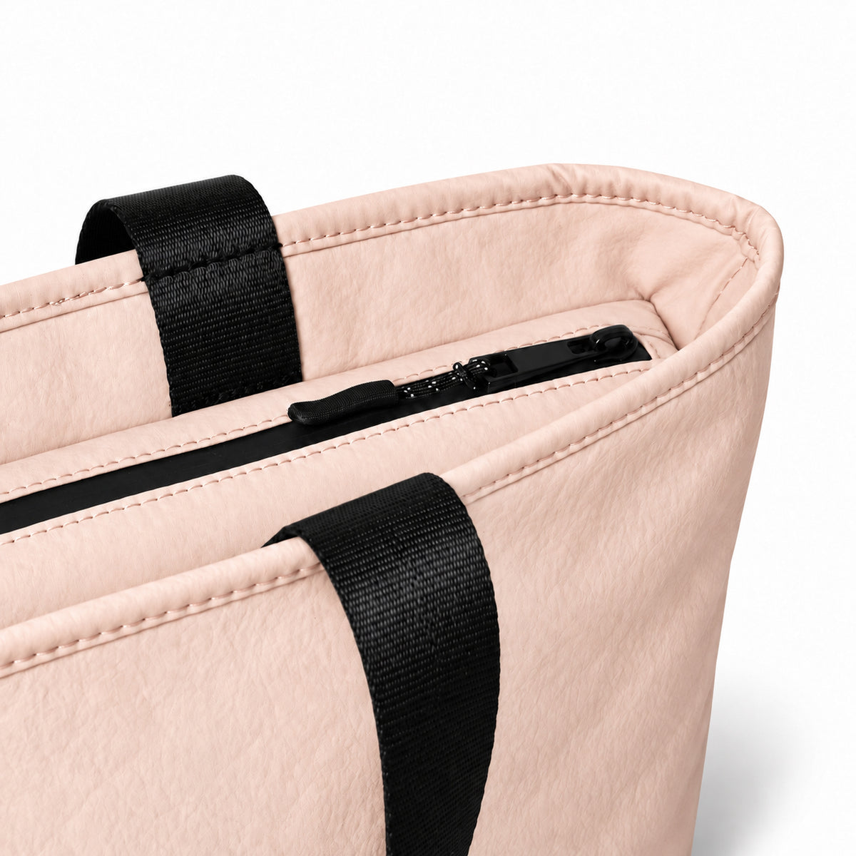 Close-up of the blush pink tote zipper, stitching and black handles.