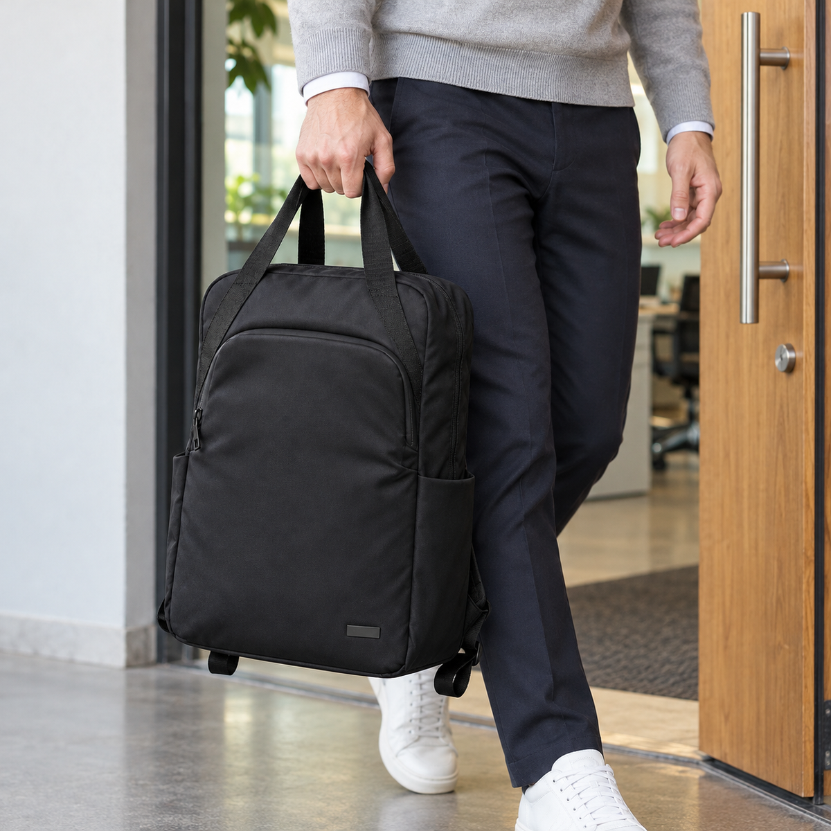 Black tote backpack carried by its two top handles at an office entrance.