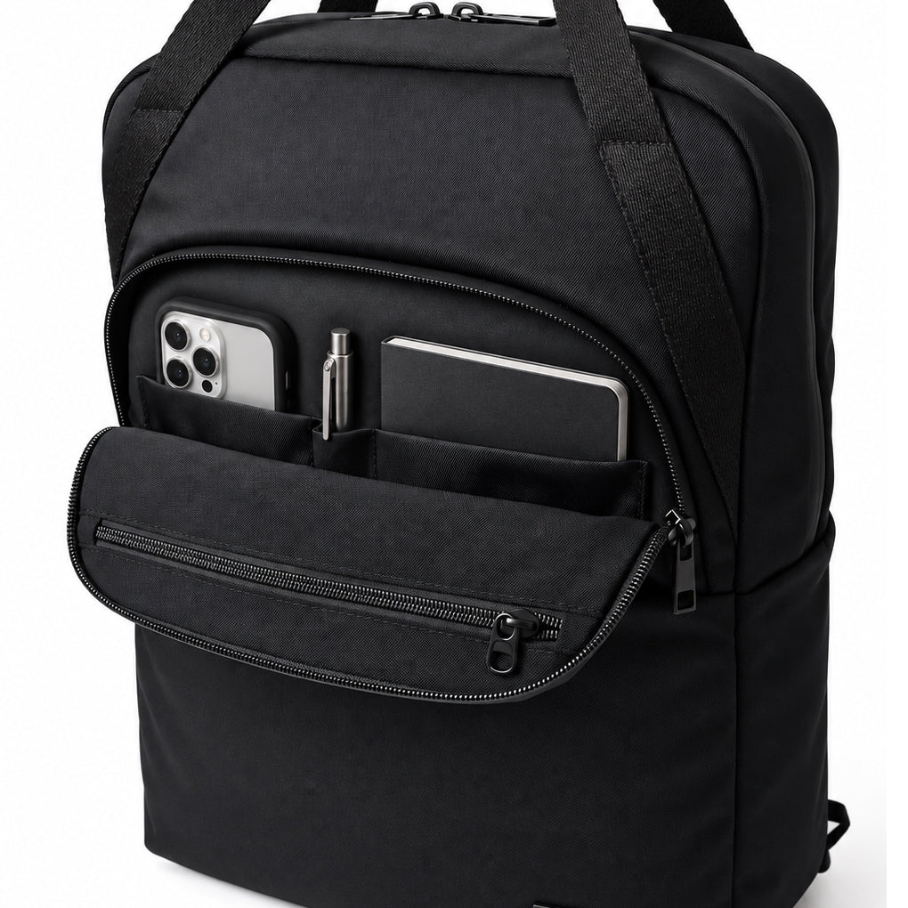 Front organizer compartment of the black tote backpack holding a phone, pen and notebook, with the inner zip pocket visible.